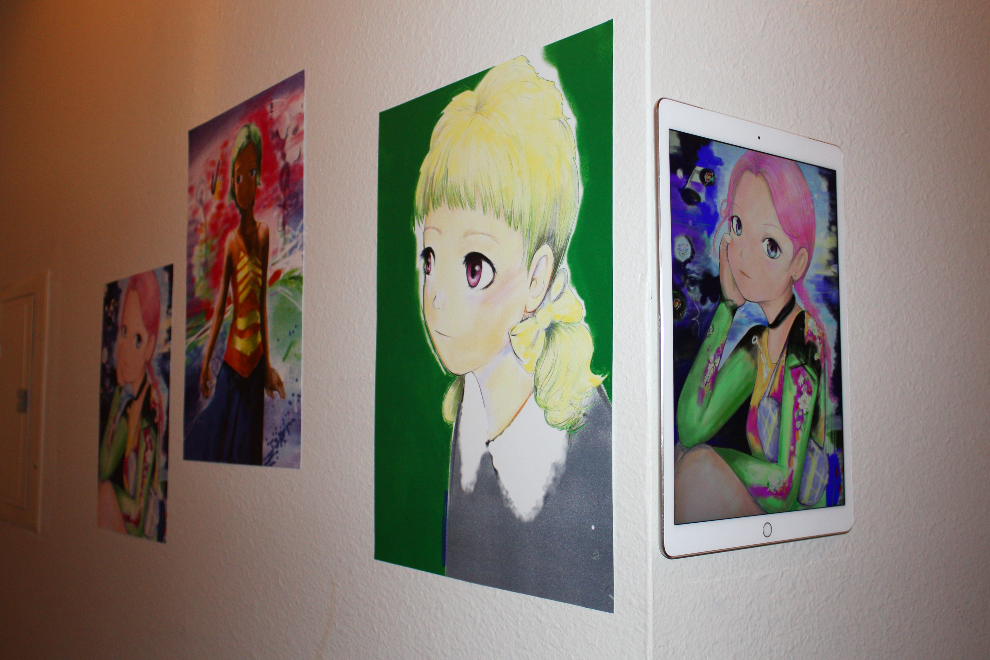 The corner of a hallway with three prints and an ipad with illustrations of anime girls hung on the wall